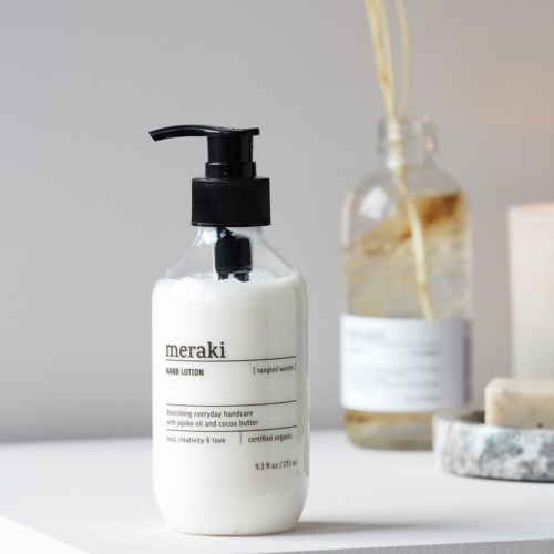 En vit flaska märkt 'Meraki hand lotion' på en vit yta, med andra flaskor och tvål i närheten.