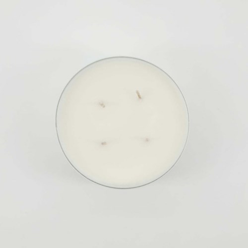 Een witte kaars in een glas met vier gebrande lonten, tegen een effen witte achtergrond.