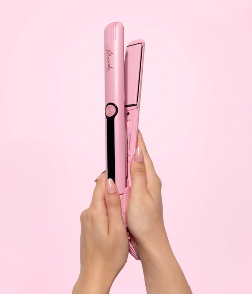 Eine Person hält ein pinkes Glätteisen vor einem pinken Hintergrund.