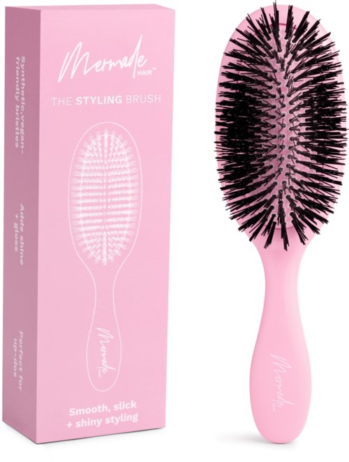 Eine pinke Haarbürste mit schwarzen Borsten neben einer pinken Verpackung, markiert 'Merade hair' und 'styling brush'.