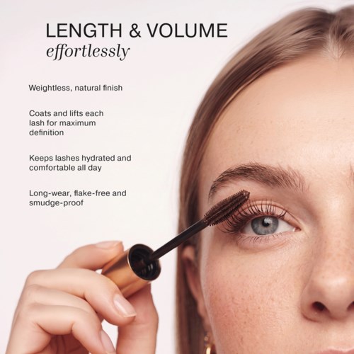 En kvinde, der påfører mascara på sine vipper med en børste, fremhæver lange og bukkede vipper. Baggrunden er lys beige.