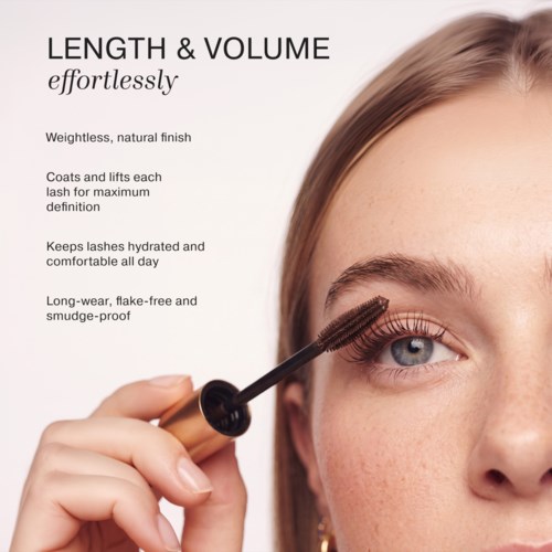 Close-up of a woman applying mascara to her eyelashes with a brown mascara wand.