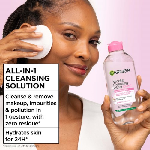 En kvinna använder en bomullspad för att rengöra ansiktet med Garnier Micellar Cleansing Water, medan hon håller flaskan i andra handen.