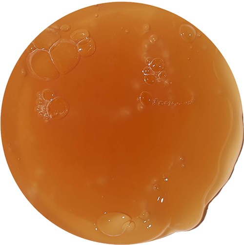 Orange vätska med bubblor på toppen, verkar tjock och skummig vid kanterna.