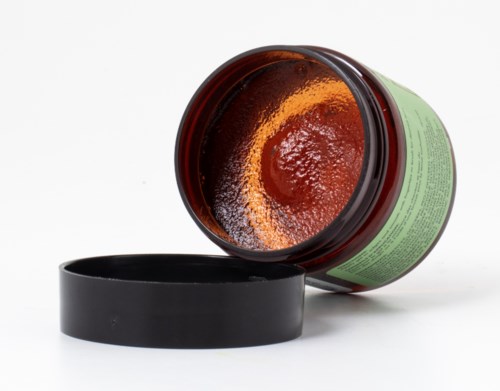 Ein offener Behälter mit rotem Paste und schwarzem Deckel daneben.