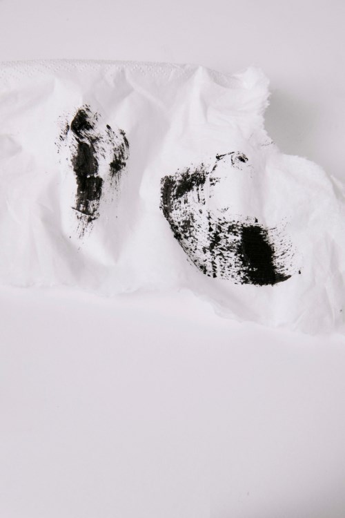 Black shoe prints on a torn white tissue or paper. Two distinct footprints are visible.