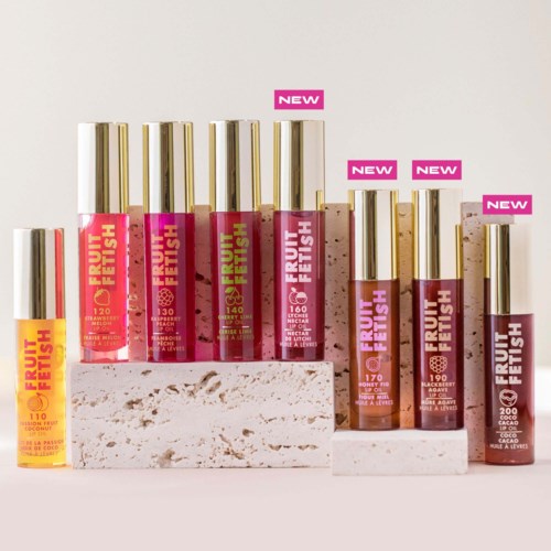 Collection of colorful lip glosses with gold caps, labeled 'Fruit Fetish' and 'NEW,' displayed on white blocks.