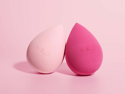 Two makeup sponges, one white and one pink, stand side by side on a pink background.