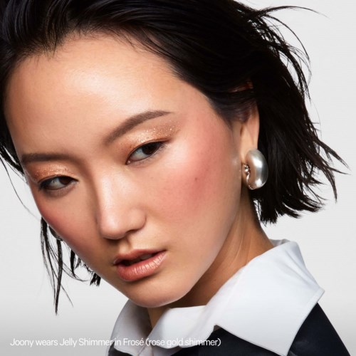 A woman with short black hair, large pearl earrings, and a white shirt, looking confidently at the camera.
