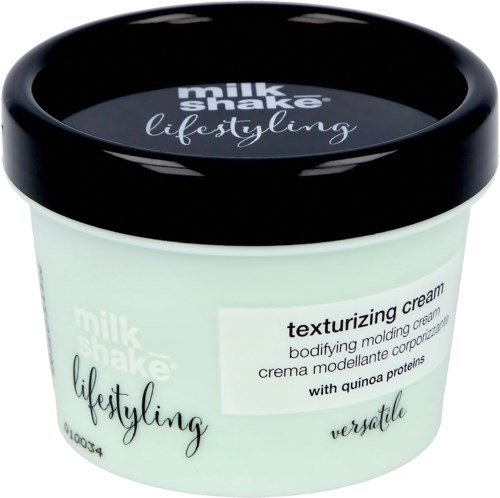 En behållare med Milk Shake texturizing cream med quinoa proteiner, svart lock och vit kropp med produktinformation.
