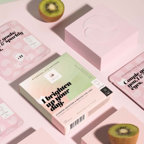 Lådor med Milus ögonpatcher och skivade kiwifrukter på rosa bakgrund, med en rosa box och utspridda förpackningar.