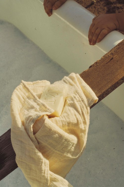 Cloth and gloves hanging on a wooden railing near a pipe or drainage area.