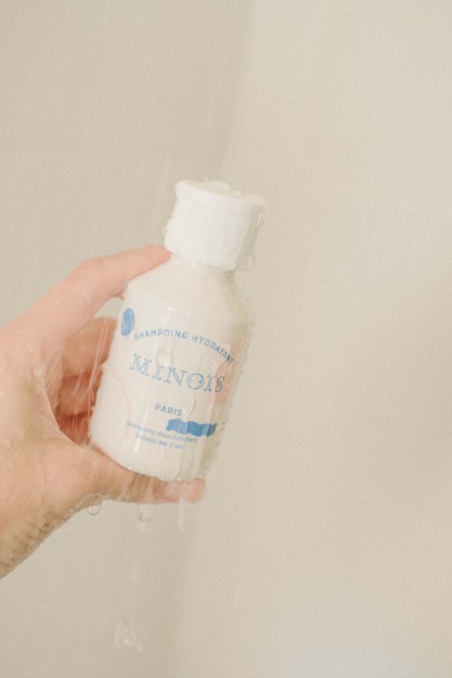 Eine Hand hält eine weiße Sprühflasche mit blauer Schrift und sprüht Wasser an eine hellfarbene Wand.