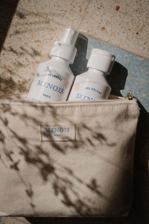 To hudpleje flasker i en beige taske, sollys og skygge skaber et naturligt mønster på tasken.