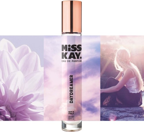 En parfymflaska märkt 'Miss Kav Daydreamer' framför en mjuk lila blomma och en flicka med långt hår som sitter vid vattnet.