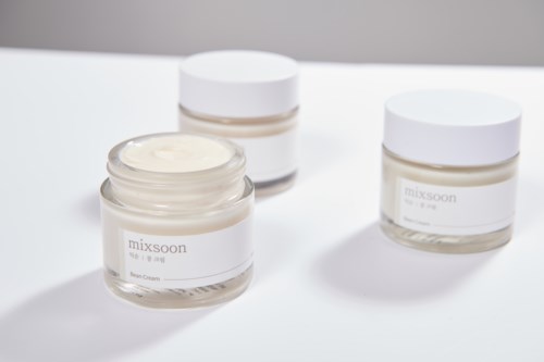 Drie potjes crème met witte deksels op een witte ondergrond, één open met de creme erin.