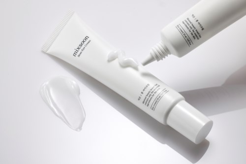 Two white tubes with cream, one squeezing out cream onto a surface, on a white background.