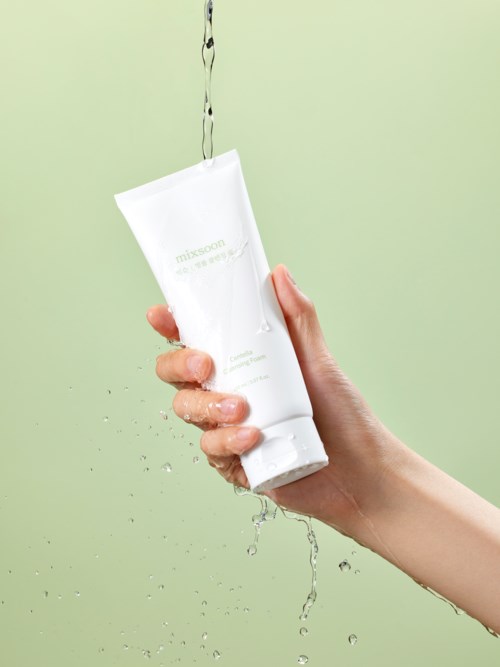 A hand holding a white tube under running water with a soft green background.