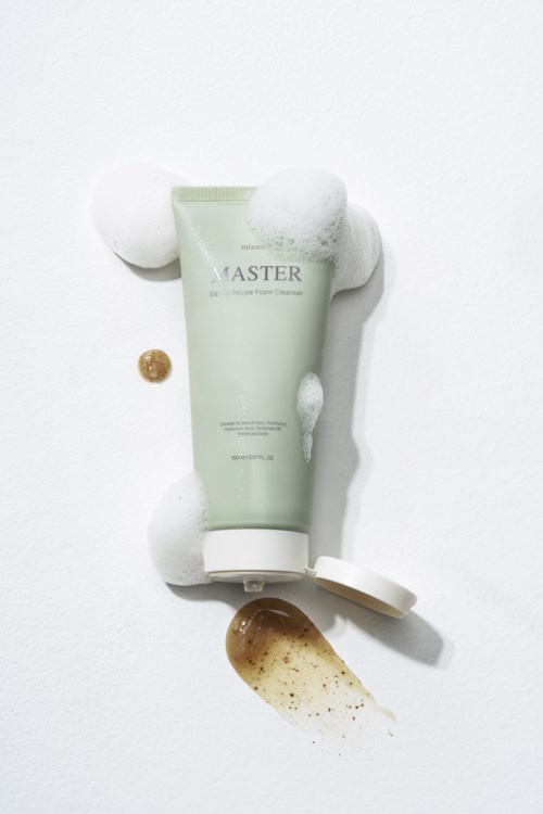 Eine Tube mit der Aufschrift 'Master' umgeben von Schaum, mit verschüttetem Produkt und kleinem braunen Objekt.