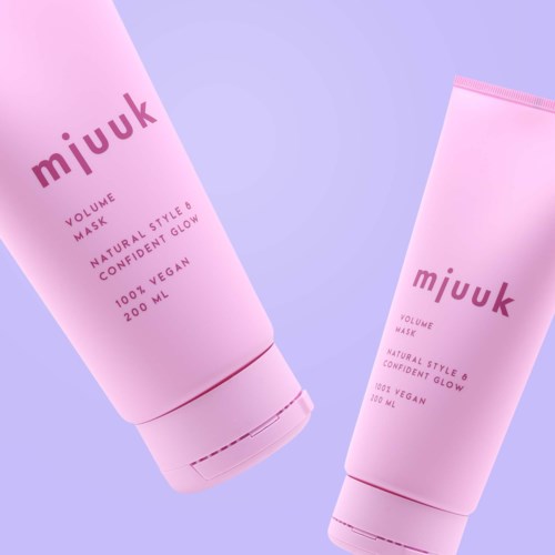 To rosa tubes merket "mjuuk" med informasjon om volum og fordeler. De står mot en pastel bakgrunn.