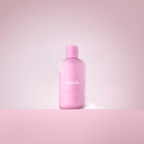 En rosa flaske med hvit etikett på en rosa overflate, med lys rosa bakgrunn.