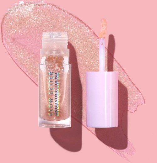 En læbepomadeflaske med blankt gyldent gloss indeni, placeret ved siden af en lyserosa læbe gloss applikator på en pink baggrund.