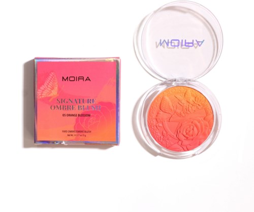 En kompakt blush med orange og pink nuancer, og dens pink emballage boks ser på en scene modsat blushen.
