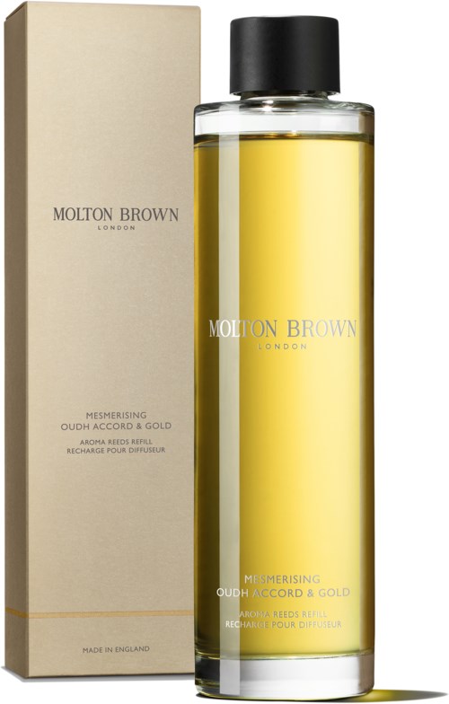 En lång glasflaska med gul vätska och svart lock, och en beige förpackning märkt Molton Brown London.