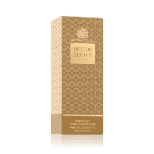 En lång låda i guld och beige färger med mönster och texten "Molton Brown" för kroppsolja.