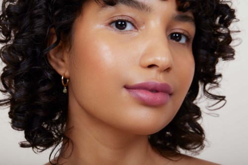 A woman with curly hair and earrings, clear skin, and soft makeup, looking at the camera.