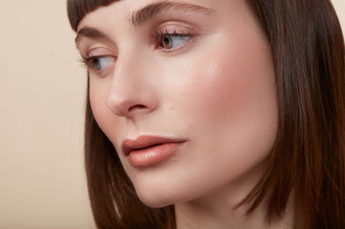 Close-up of a woman with smooth skin, brown hair, and light makeup looking to the side.