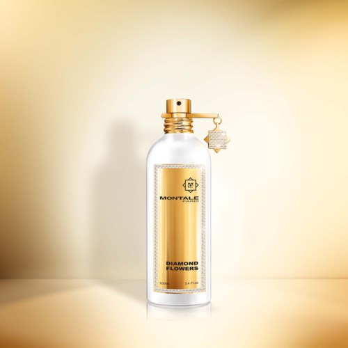 Eine klare Parfümflasche mit Goldakzenten und einem Diamantenblumen-Etikett, steht vor einem neutralen Hintergrund.