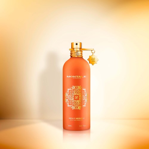 A red-orange perfume bottle with a gold spray cap and a small star ornament hanging from it.