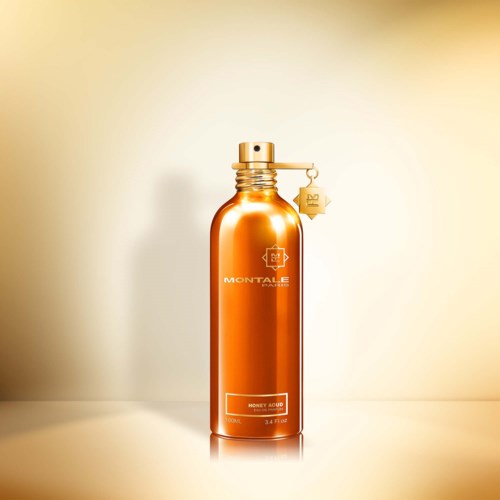 Eine glänzende, orangefarbene Flasche mit goldener Kappe und Anhänger, beschriftet mit 'Money Acid' und 'Montale'.