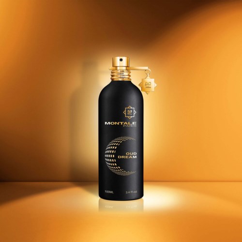 A black perfume bottle with gold lid and tag, labeled 'Montale Paris Oud Dream,' stands on a yellow surface.