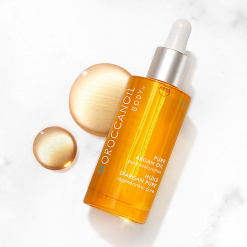 En flaska Moroccanoil Body med pipett, placerad på en vit yta med två droppar bredvid.