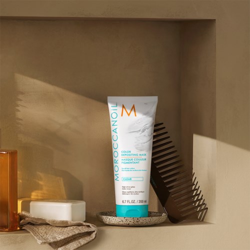 En tube med Moroccanoil fargedeponeringsmaske på en liten tallerken, med en kam og en såpe i nærheten.