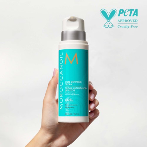 Dłoń trzyma butelkę Moroccanoil Curl Defining Cream w kolorze niebiesko-białym, oznaczoną jako cruelty-free i zatwierdzoną przez PETA.