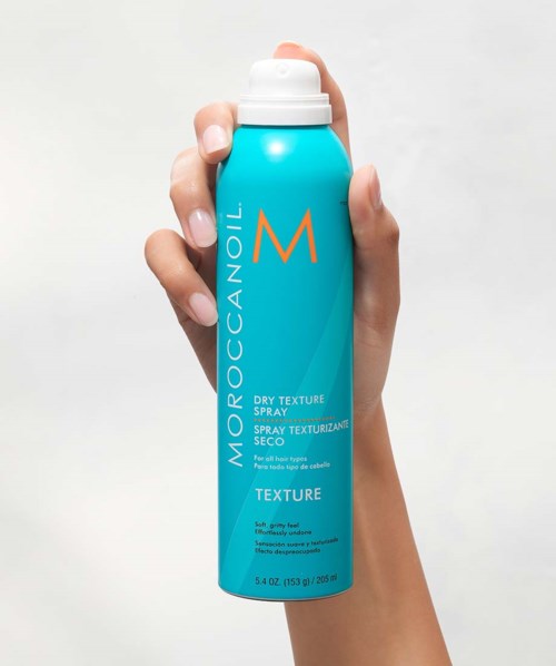 En hand håller i en blå burk med Moroccanoil torrspray mot en vit bakgrund.
