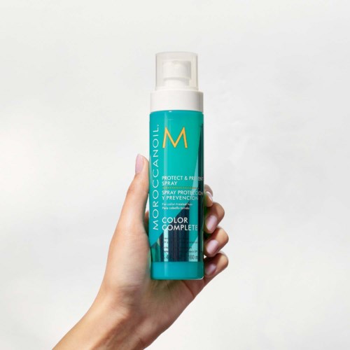 En hand håller en blå och vit sprayflaska märkt Moroccanoil Color Complete Protect & Prevent.