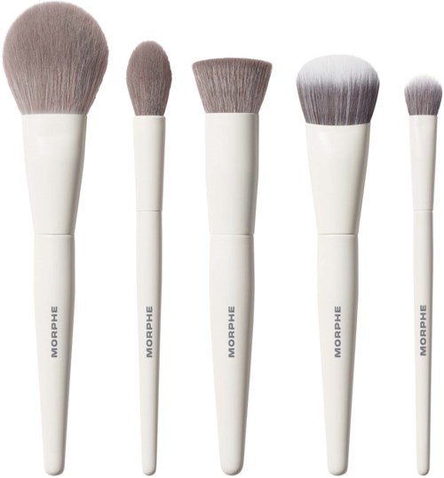 Five makeup brushes with varying sizes and shapes are lined up, all with white handles and soft bristles.