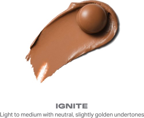 Ett brunt makeupproduktfläck med en rund topp, skrynkligt på en vit bakgrund, märkt IGNITE med ljus till medium nyans.