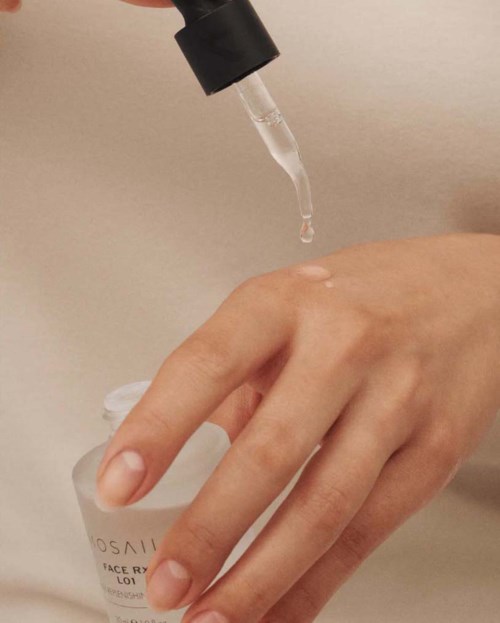 A hand holding a small white bottle with a droplet of liquid falling from a dropper.