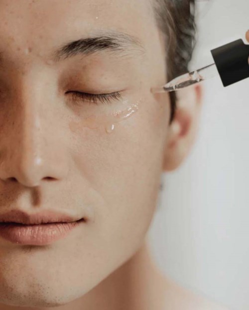 A person has liquid being applied to their under-eye area using a dropper.