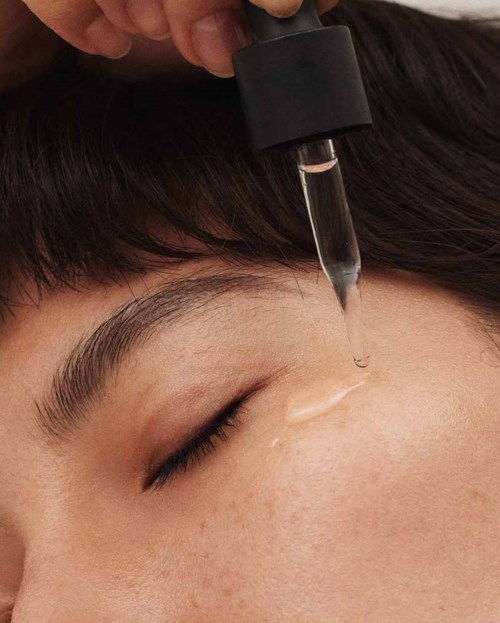 A person receives skincare treatment with a dropper applicator on their forehead.
