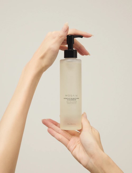 Two hands hold a beige bottle with a black pump, labeled MOSAIC Gentle Purifying Cleanser.
