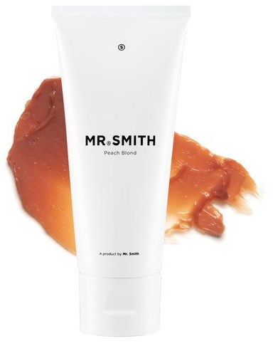 En hvit tube merket 'MR SMITH Peach Blond' med ferskenfarget sminke i bakgrunnen.