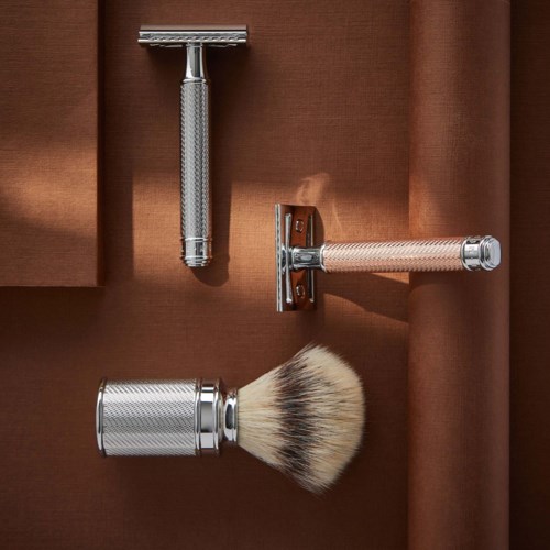 A safety razor, shaving brush, and razor holder on a brown background. The razor holder has a horizontal bar.