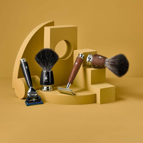 Zbiór narzędzi do golenia, w tym maszynka do golenia, pędzel do golenia, safety razor i szczotka do pielęgnacji na beżowym geometrycznym tle.
