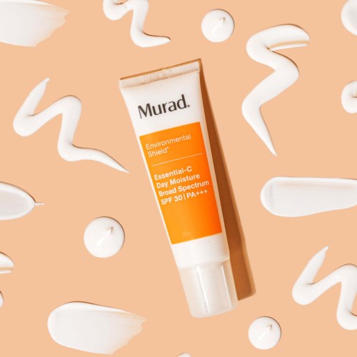 En tube med Murad Environmental Shield solkrem omgitt av hvite kremvinger på en ferskenbakgrunn.